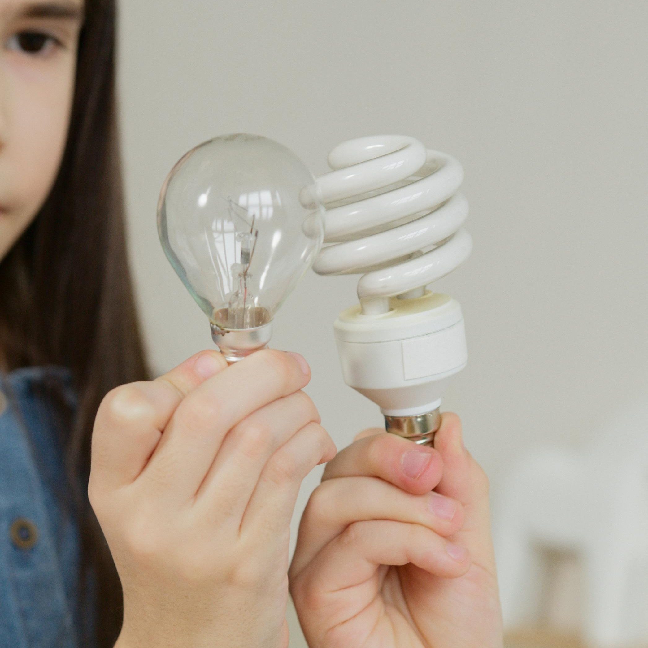A person comparing two different light bulbs to decide which one to choose